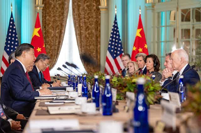 A large table with a Chinese and US delegation. Presidents Xi and Biden sit opposite each other.