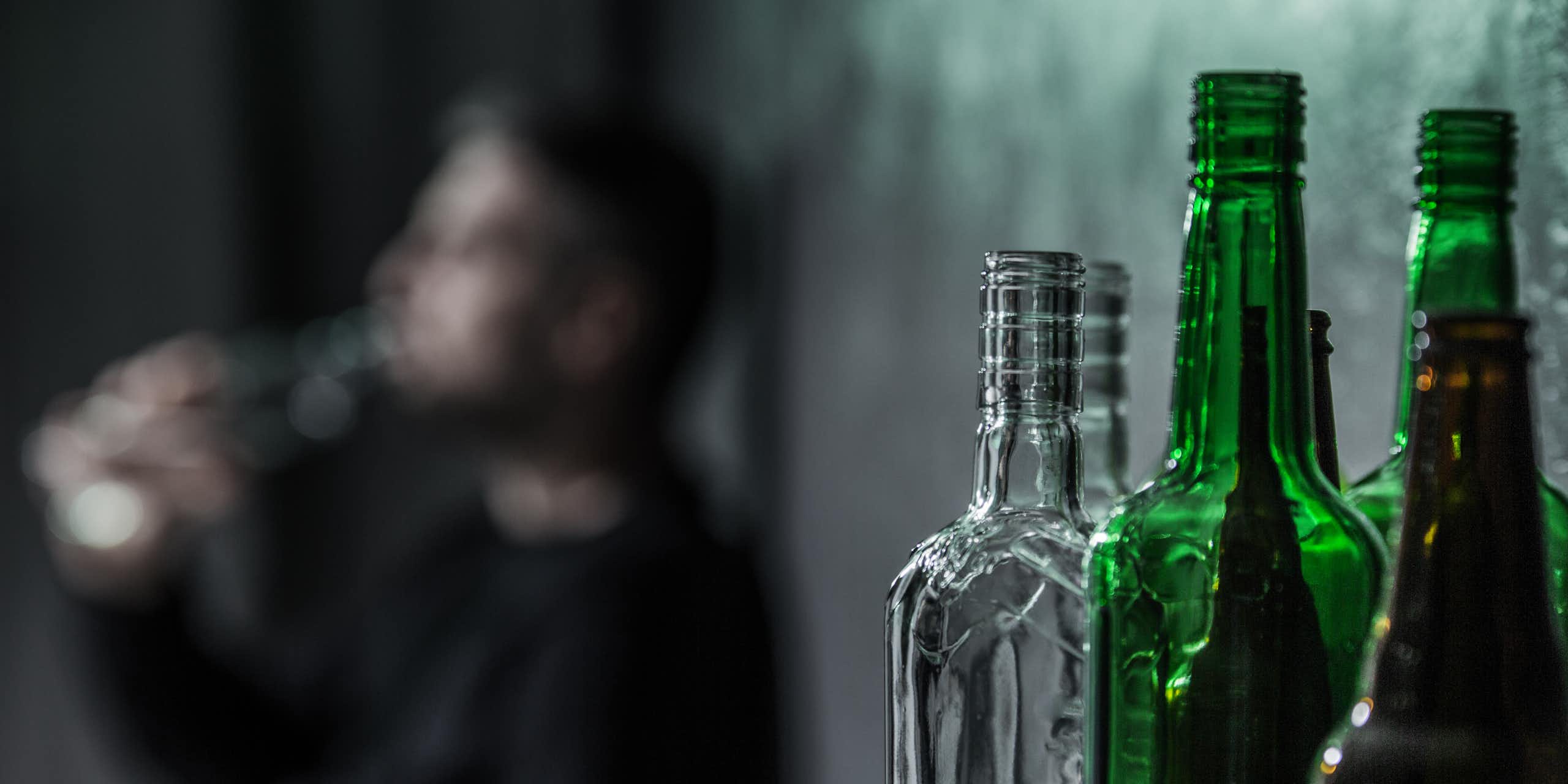 Man drinking from a bottle of alcohol, with more empty bottles in the foreground.