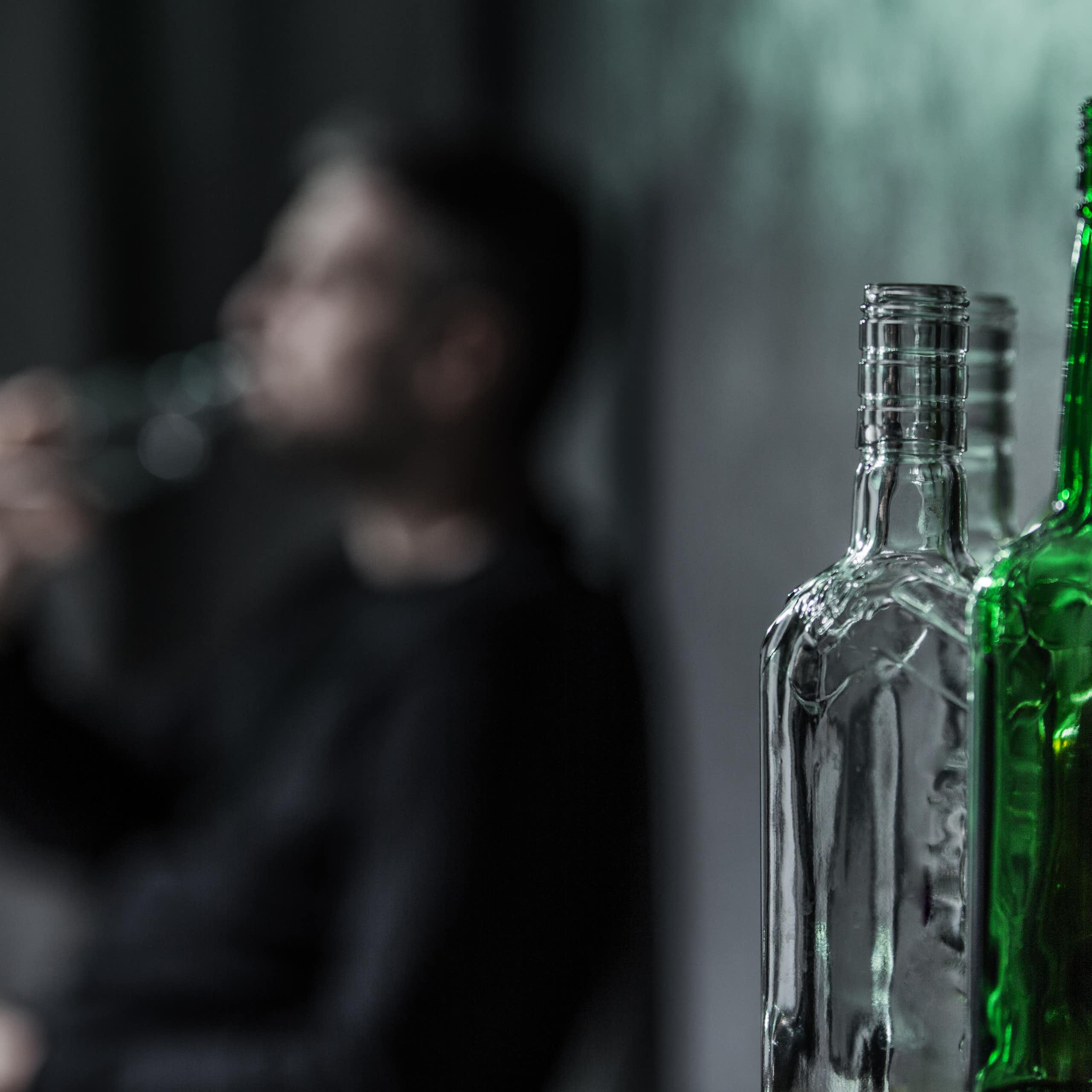Man drinking from a bottle of alcohol, with more empty bottles in the foreground.
