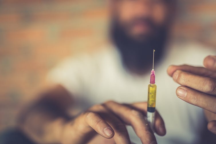 Out-of-focus man holding a syringe in the foreground