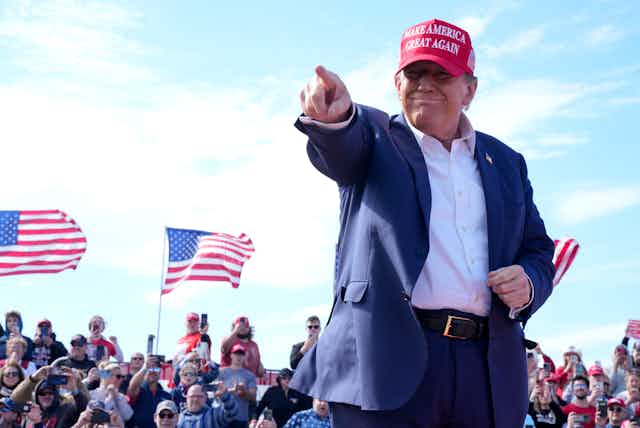 Donald Trump wears a red cap and points at the crowd during a rally