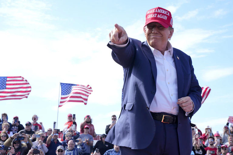 Donald Trump wears a red cap and points at the crowd during a rally