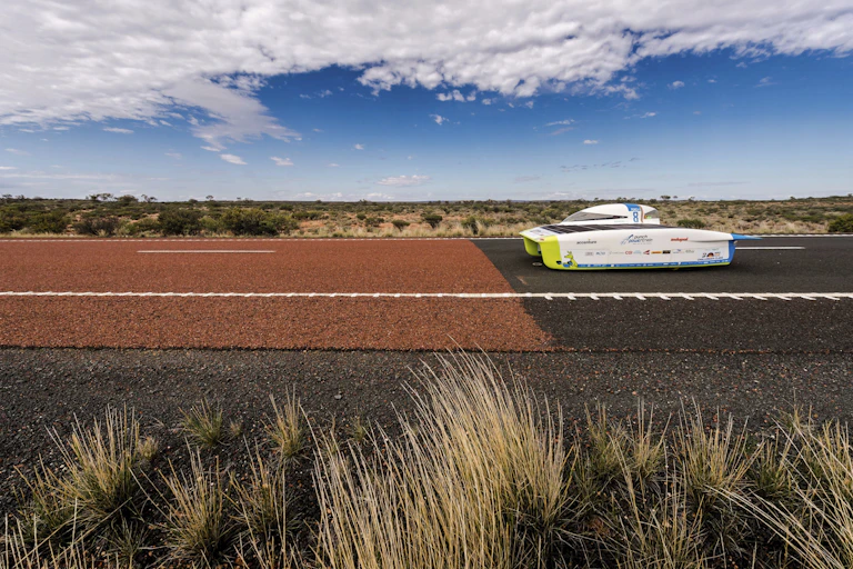 A white vehicle with a long, low dome moves along a red highway