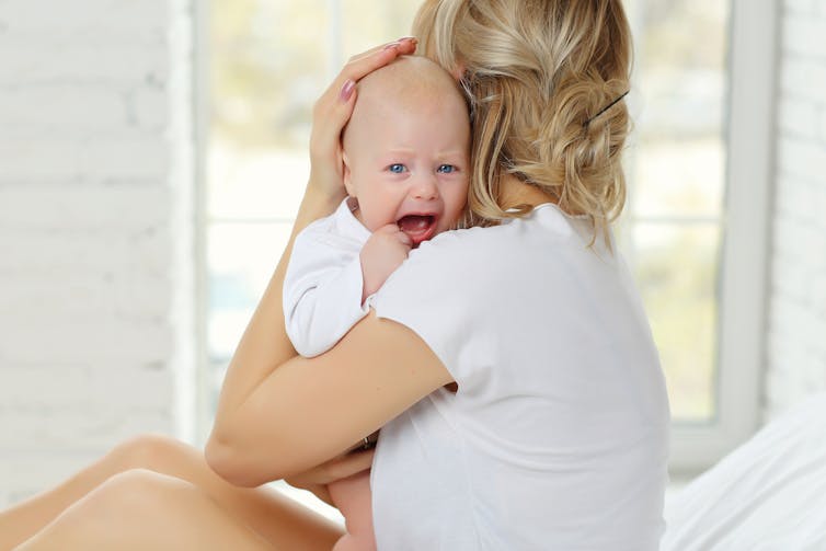 Woman looking out a window while holding a crying baby