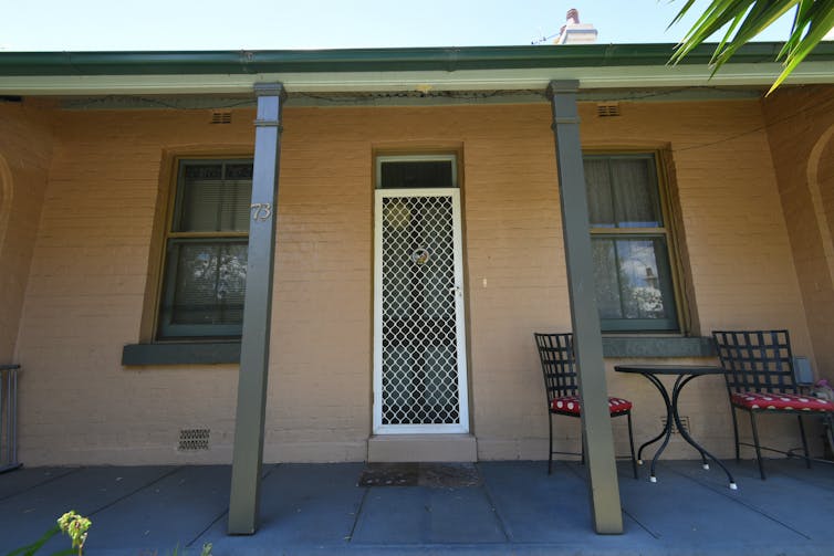 A small, brown terrace house with two pillars and a screen door