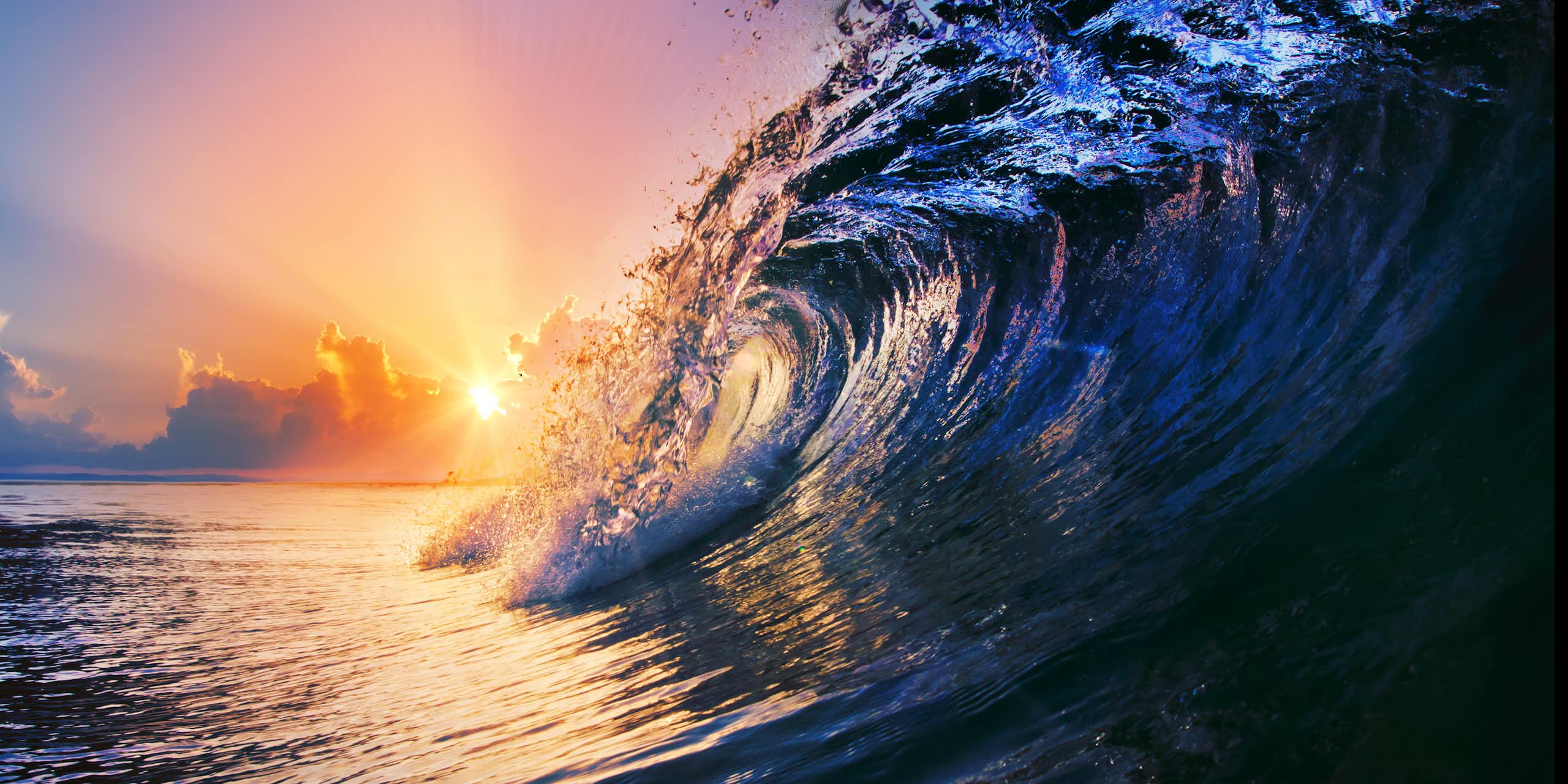 Low angle view of an ocean wave breaking with a pastel sunset in the background.