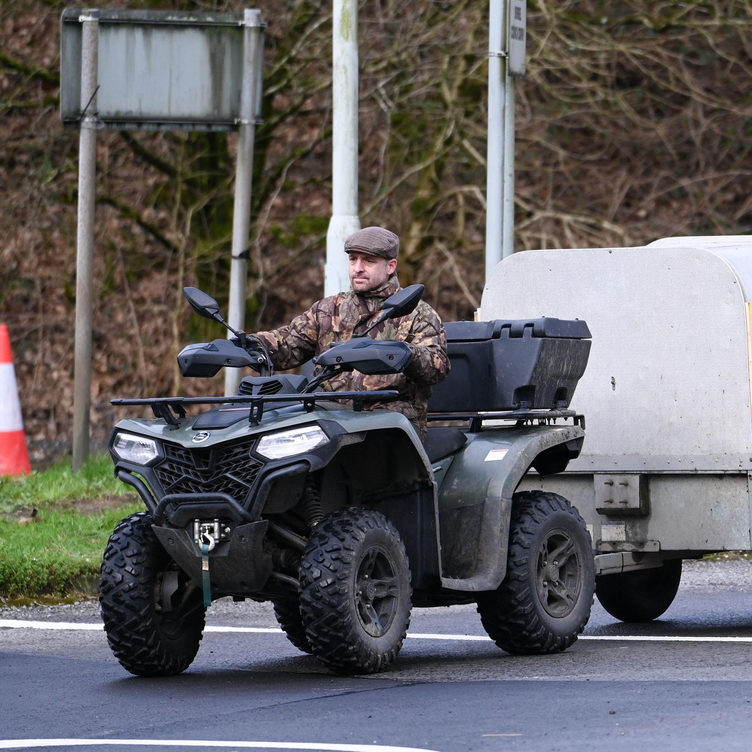 A man driving a quad bike, pulling a trailer with a sign on it that reads 'no farmers, no food'.