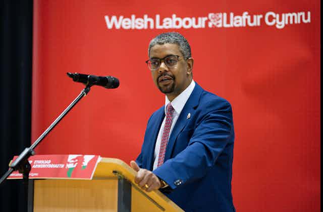Vaughan Gething standing behind a lectern with the words 'Welsh Labour Llafur Cymru' in the background. 