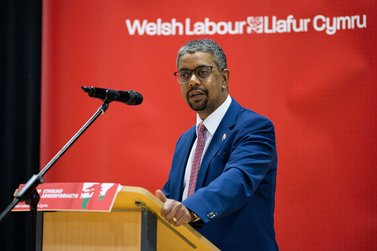 Vaughan Gething standing behind a lectern with the words 'Welsh Labour Llafur Cymru' in the background.