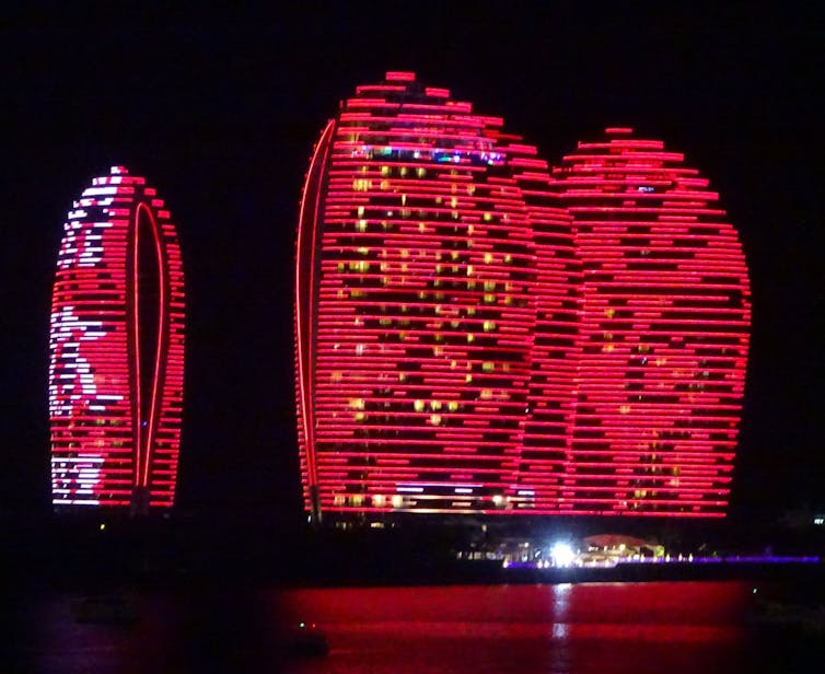 Three oval-shaped towers lit up in red at night.