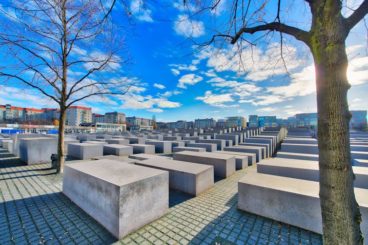 View of the memorial, rows of gray concrete slabs in a city square, stretching out against a blue sky