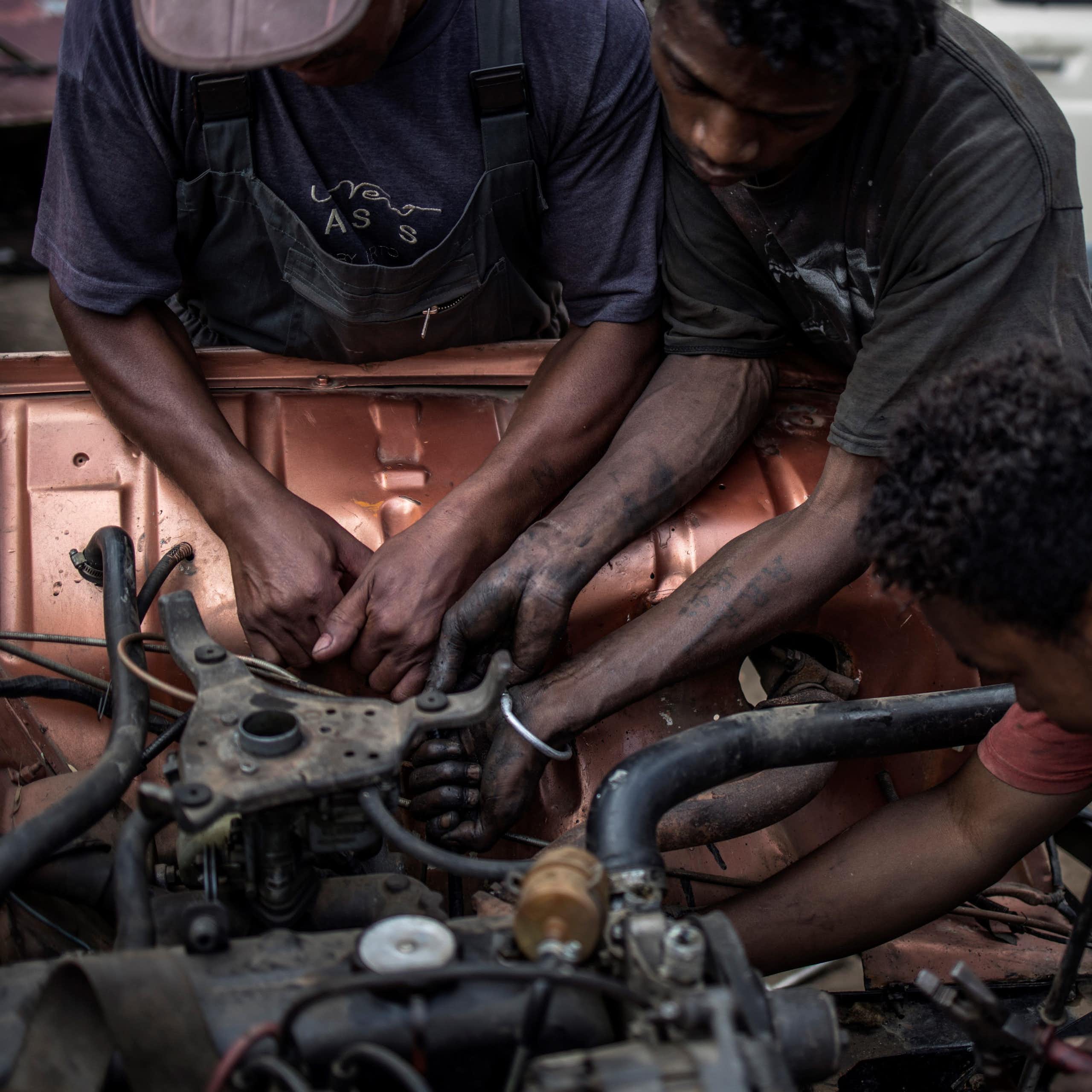 Young mechanics work on the engine of a car.