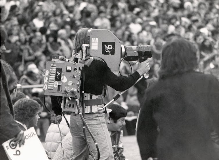 In a black-and-white image, an NBC cameraman is seen filming a Rose Bowl game in Pasadena, California, in 1970.