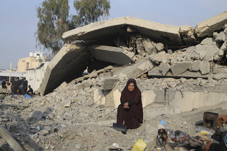 A woman sits outside a destroyed home.