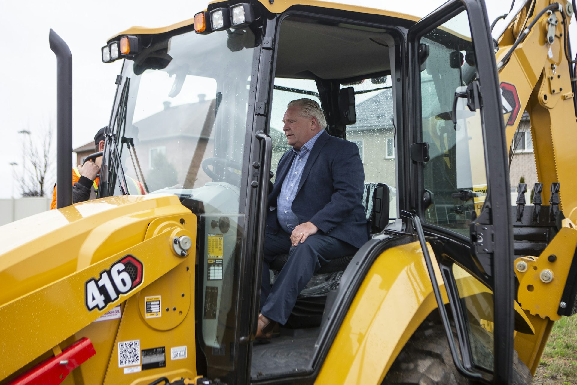 A rotund man with slicked-back greyish blond hair sits in the cab of a bulldozer.