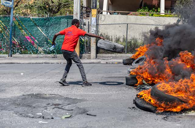 A man holds a tire as he places it on a pile of burning tires.