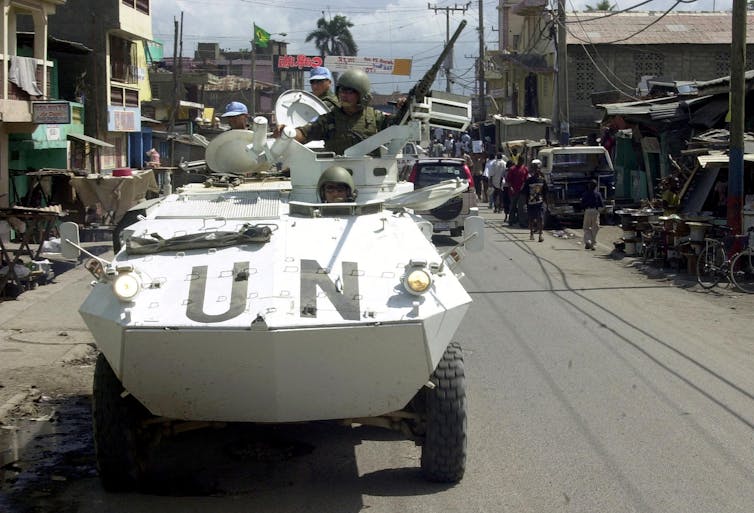 A tank painted white with UN written on it drives down the street.