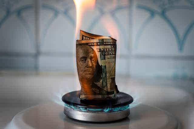 A 100 dollar bill set aflame on a gas stove.