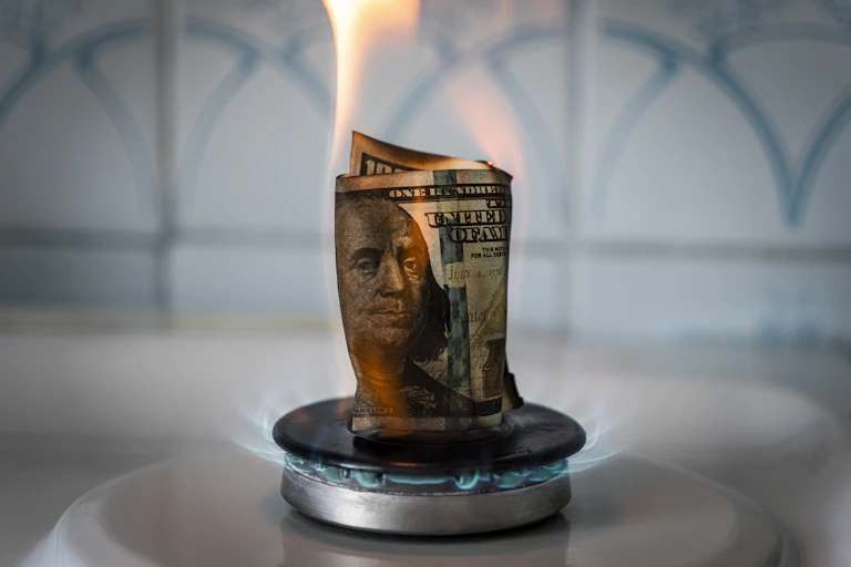 A 100 dollar bill set aflame on a gas stove.