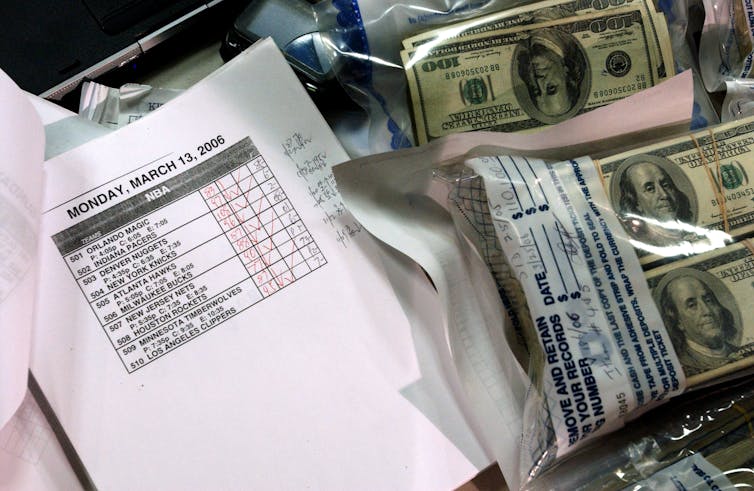 Bags of cash and printout of a March Madness schedule are seen on a police evidence table.