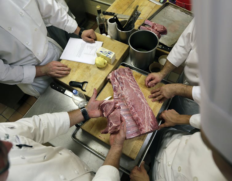 A bird's eye view: Culinary students stand around a piece of pork while an instructor demonstrates how to cut the meat.
