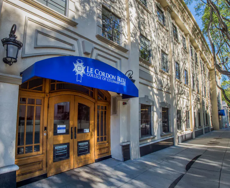 Blue awning hanging over entrance to three story building reads 'Le Cordon Bleu College of Culinary Arts.'