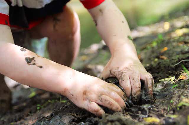 A small child's fingers dig into muddy ground.