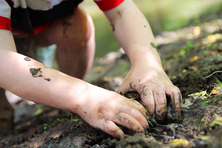 A small child's fingers dig into muddy ground.