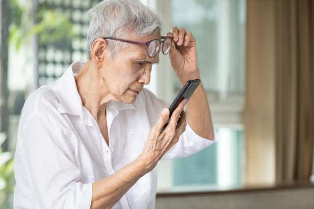 older person lifts eyeglasses to peer at phone