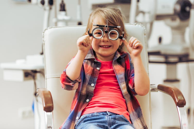 young child in clinical chair with corrective test lenses on, smiling