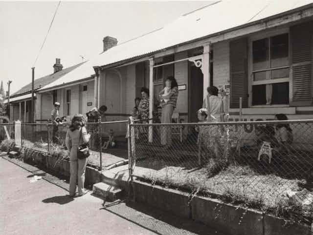Women and small children gather around a small terrace house in the 1970s