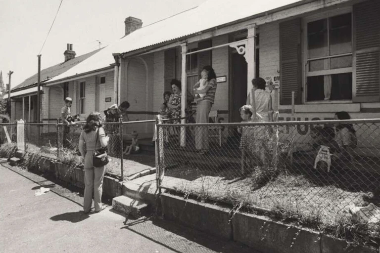 Women and small children gather around a small terrace house in the 1970s