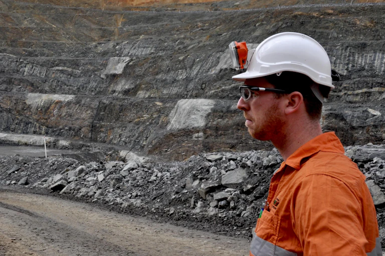 A photo of a man in high viz and a helmet standing in an open pit mine.