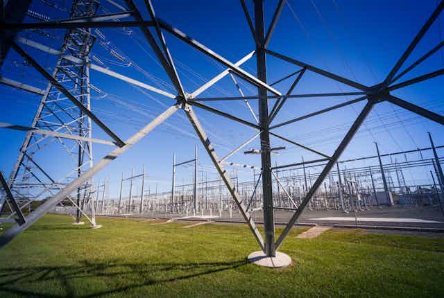 Peering through the metal structure of an electricity pylon into a power substation in Queensland, standing on green grass with a blue sky in the background