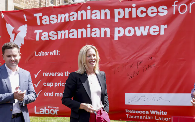 Two people in front of a large red banner reading