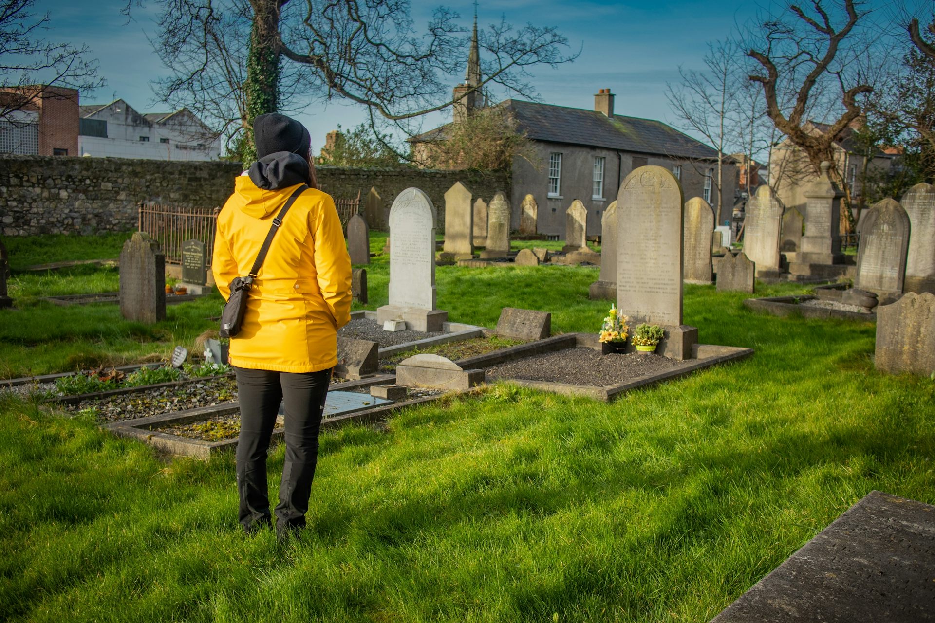 A lady in a yellow jacket stands in a cemetary.
