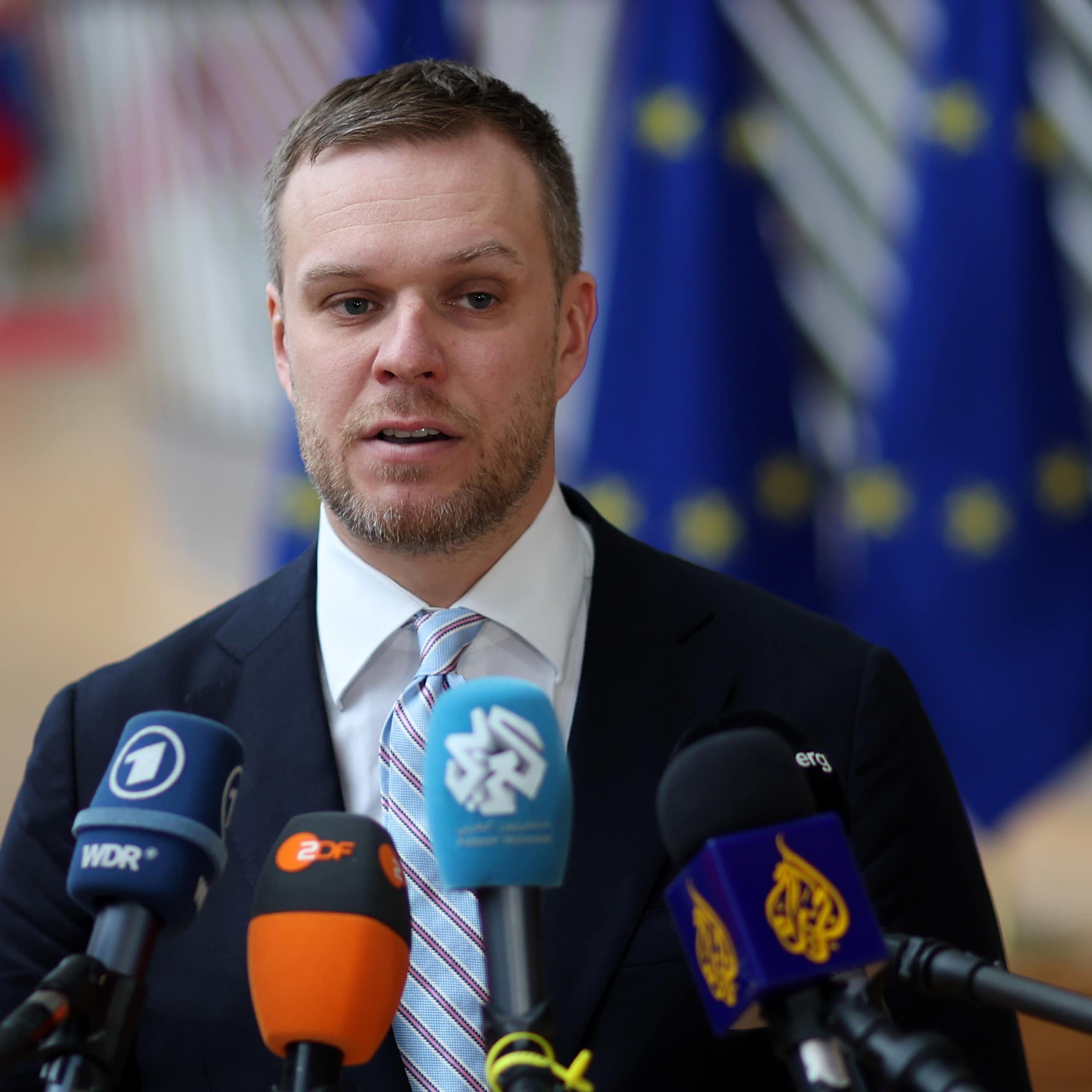 Gabrielius Landsbergis speaking into multiple microphones at a press conference with European flags in the background.