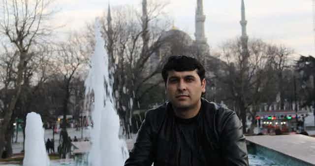 A man wearing a leather jacket is seen in front of a fountain