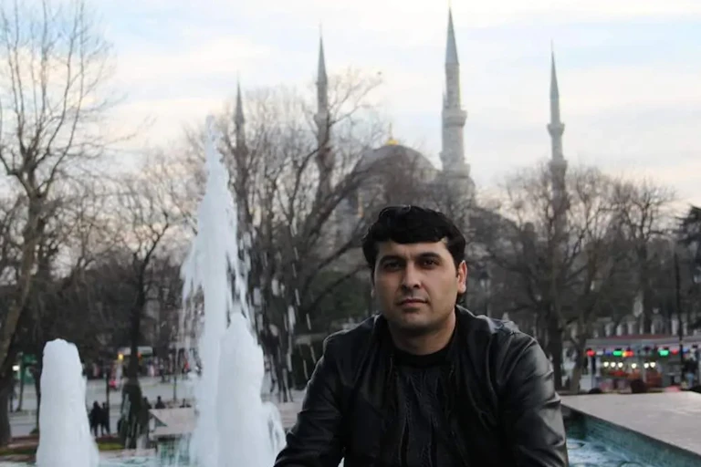 A man wearing a leather jacket is seen in front of a fountain