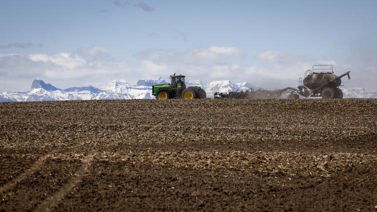 Tractors are seen on a dry farm field against a backdrop of mountains.