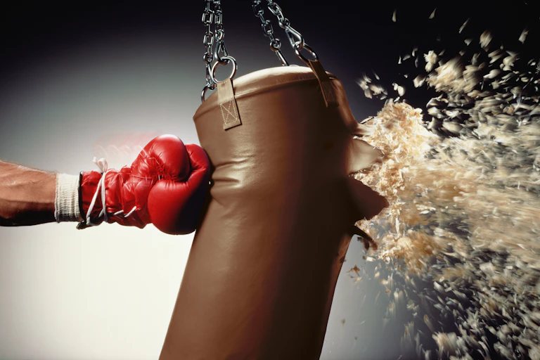 hand in boxing glove punches stuffing out of a heavy bag