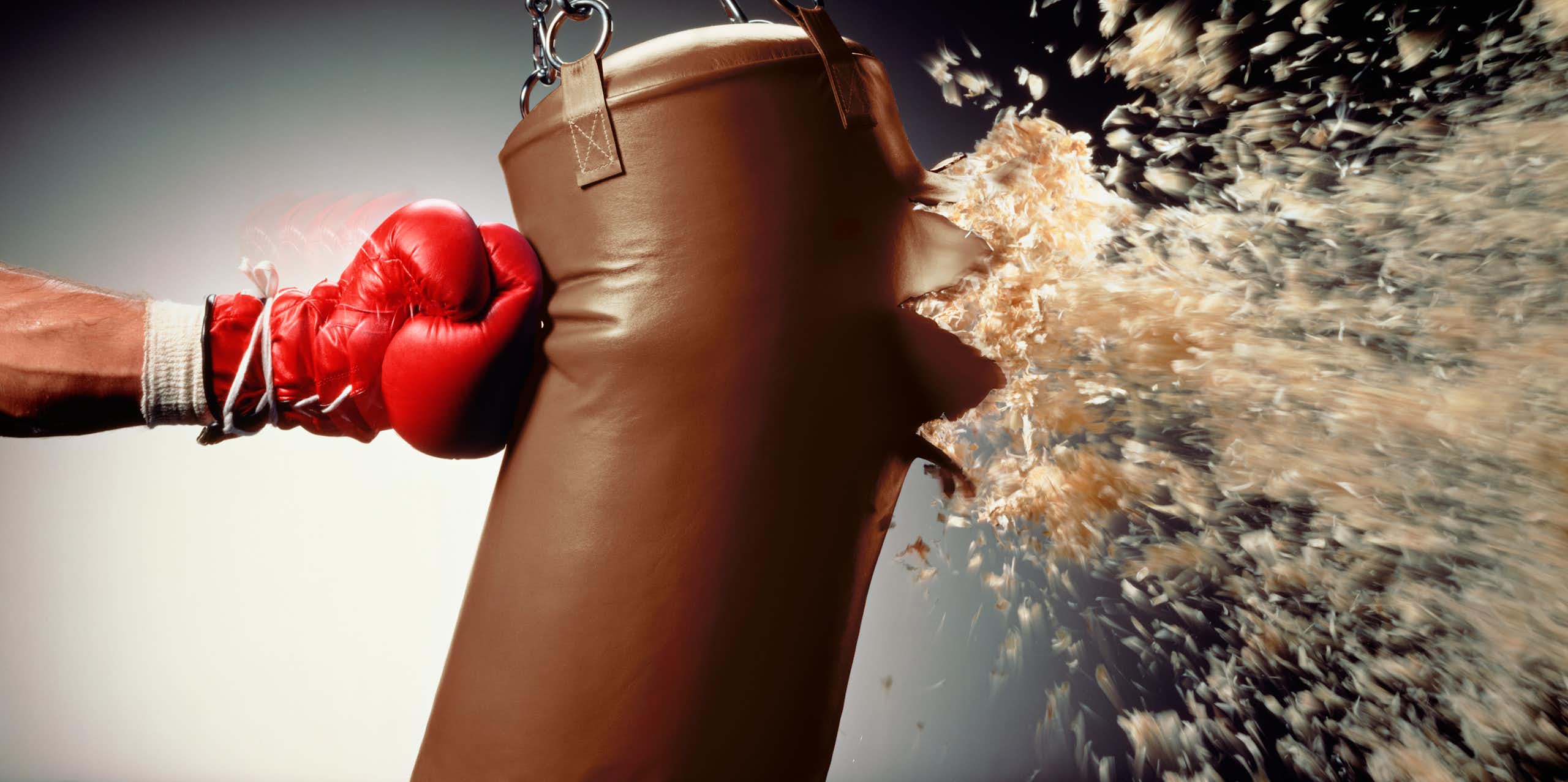 hand in boxing glove punches stuffing out of a heavy bag