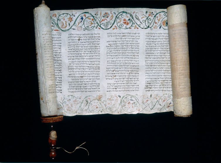 An open scroll shows text with a colored floral pattern at the top and bottom of the manuscript.