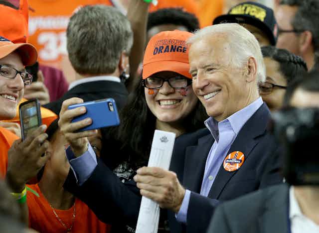 A gray haired man taking a selfie with a woman in an orange baseball cap.