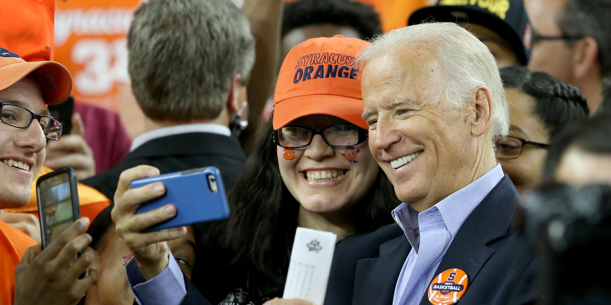 A gray haired man taking a selfie with a woman in an orange baseball cap.
