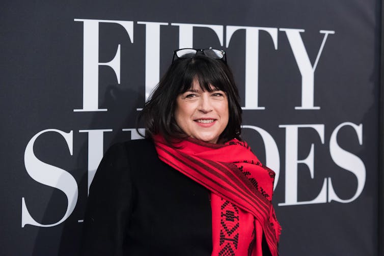 A woman in a black shirt and red scarf stands in front of a sign that says 'Fifty shades.'