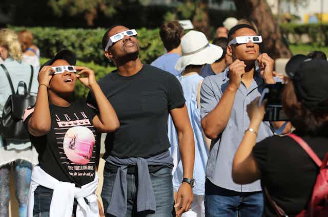 A group of people wearing eclipse glasses look up