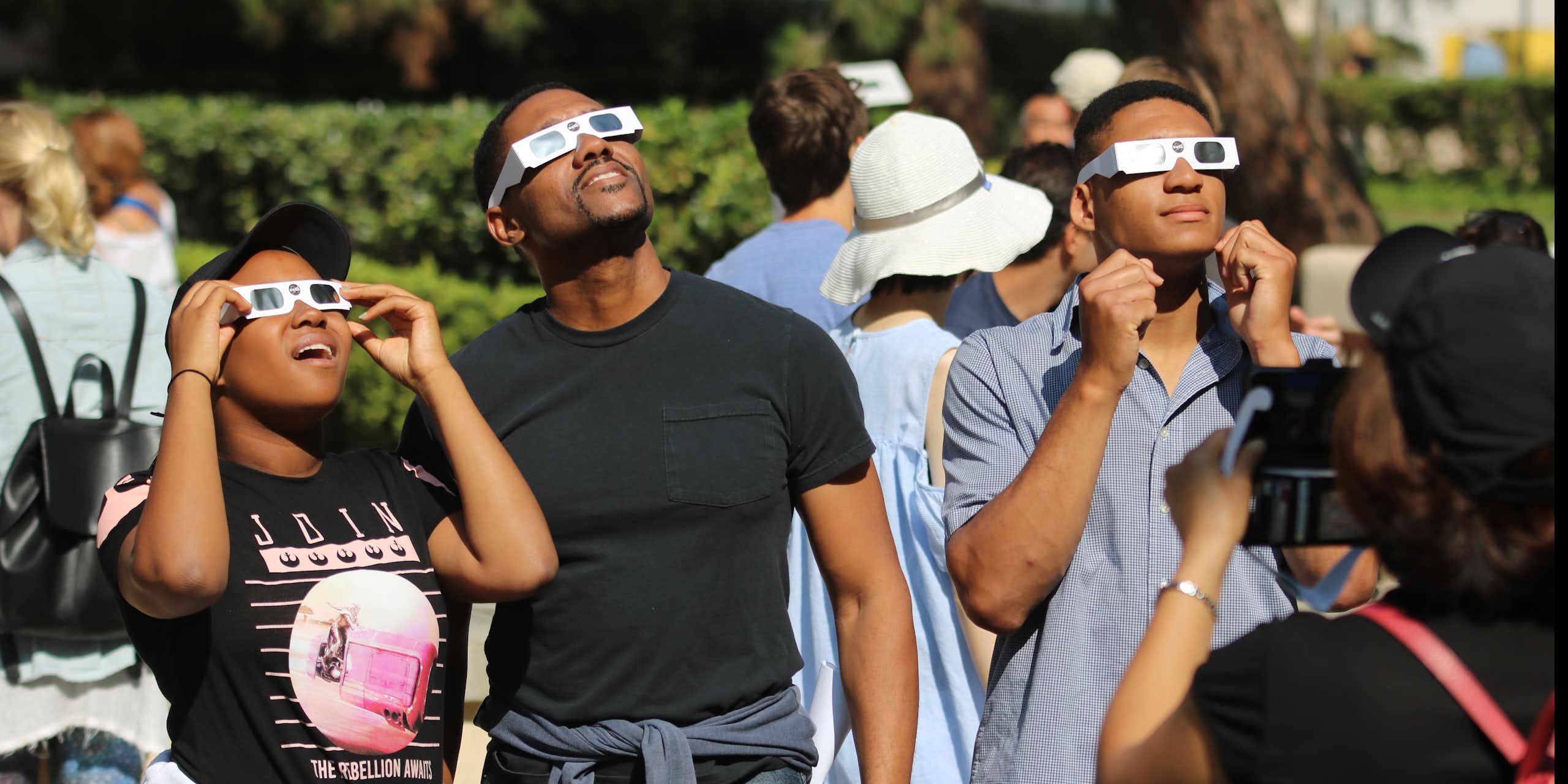 A group of people wearing eclipse glasses look up