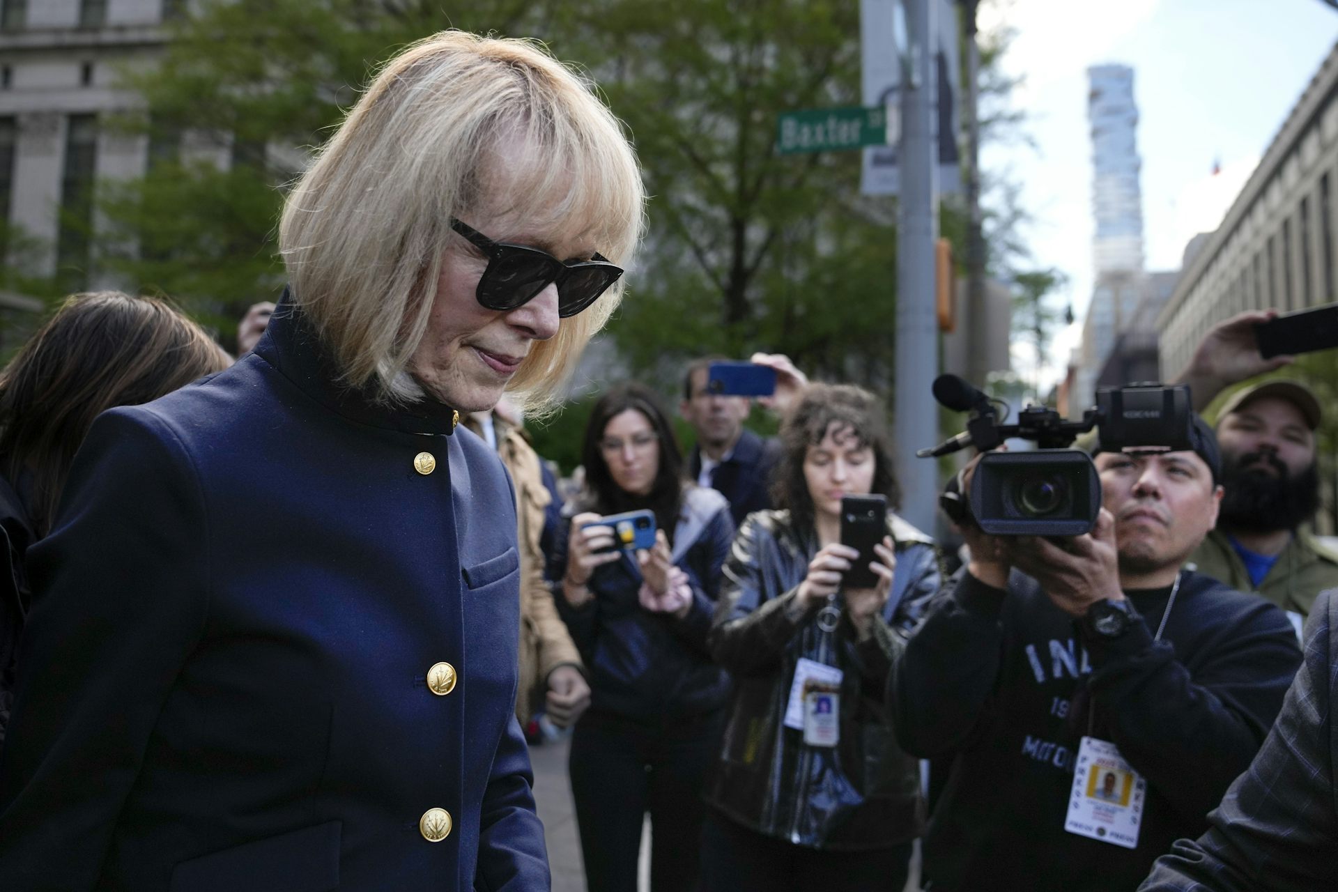 A crowd of people take photos of a middle-aged woman with a short bob haircut and sunglasses