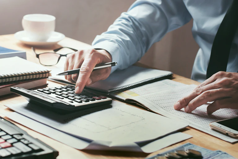 A close-up of someone's hands pushing buttons on a calculator at a desk